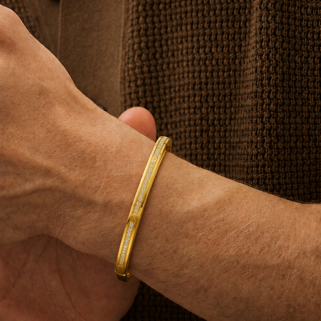 A yellow gold hinged bangle bracelet featuring the word BVLGARI engraved twice around the flat circular face, with rows of small diamonds lining the outer edge.