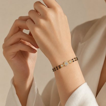 A yellow gold bracelet featuring two rows of small black beads connected to a central round diamond halo charm flanked by two gold triangle accents.