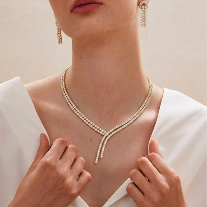 A yellow gold necklace made of two rows of small diamonds that cross over each other in the front with hanging ends.