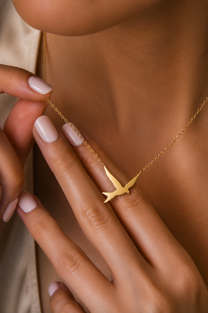 A yellow gold pendant necklace shaped like a flying swallow bird with a smooth, polished finish.