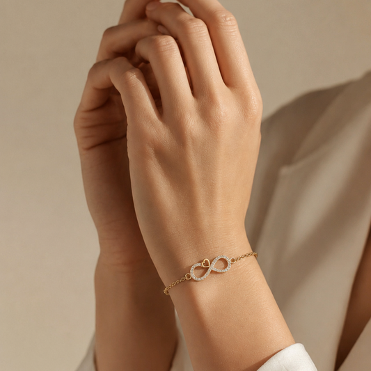 A yellow gold chain bracelet featuring a central infinity symbol lined with small diamonds and accented by a tiny open gold heart.