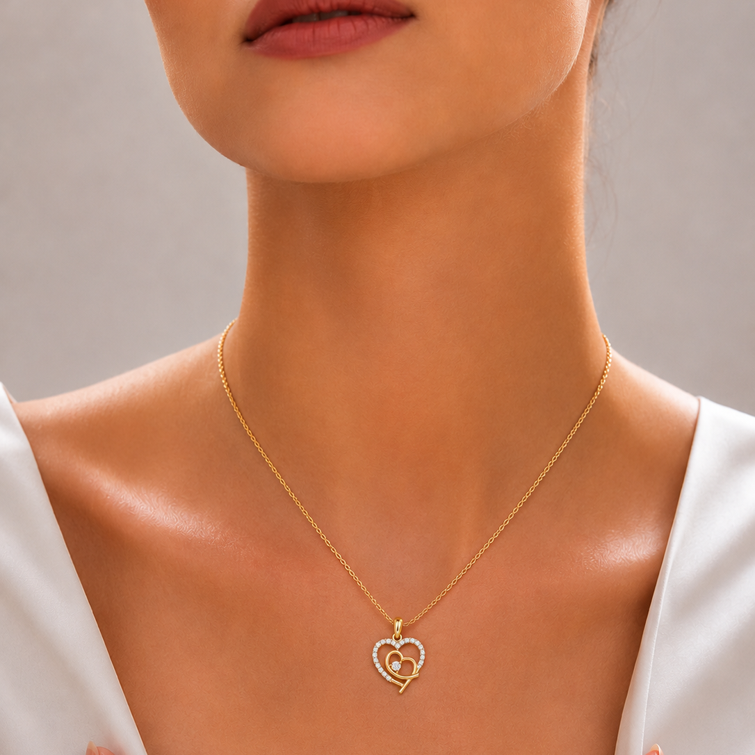 A yellow gold chain necklace featuring an open heart-shaped pendant outlined in small white diamonds, layered with a smaller interlocking smooth gold heart charm at its center.