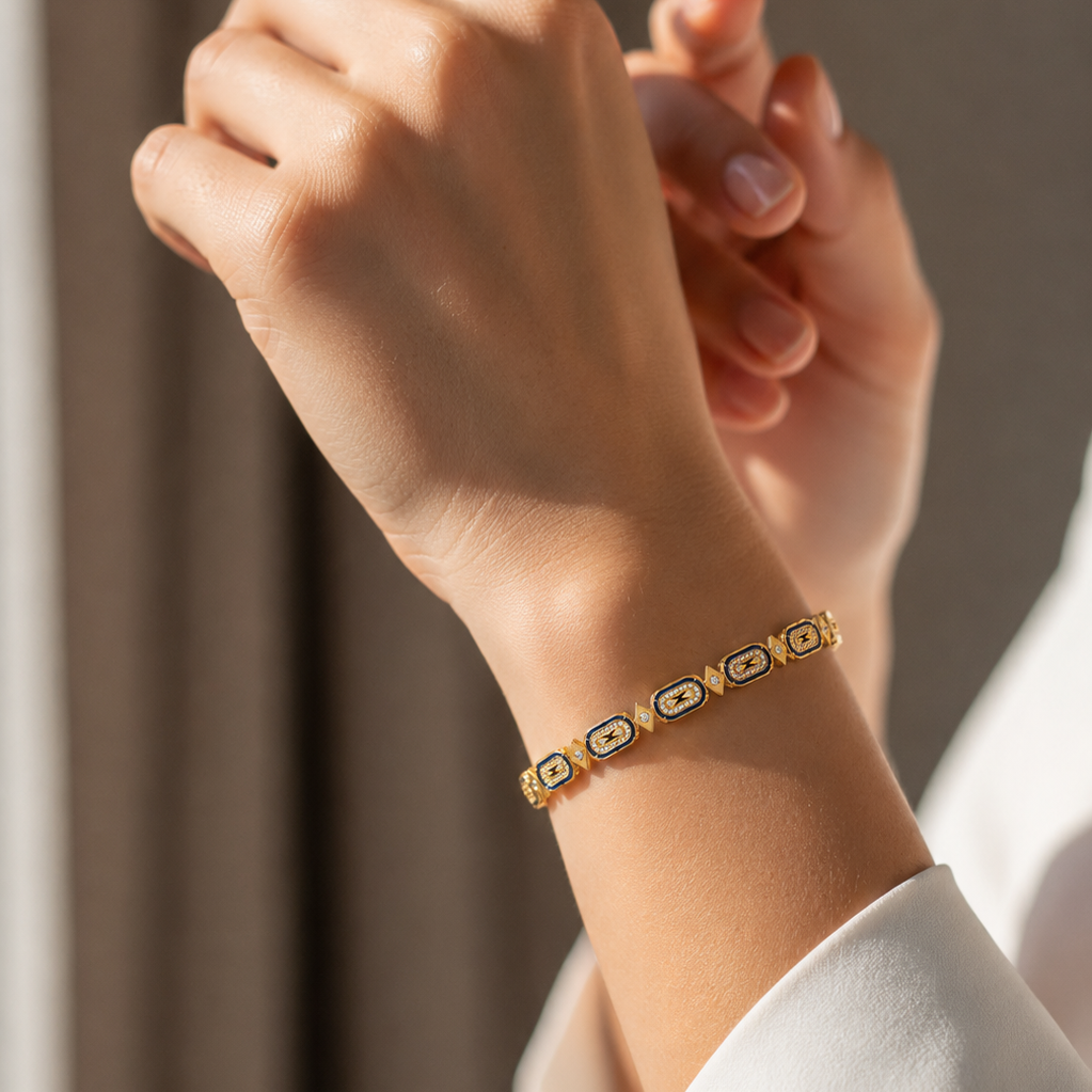 A yellow gold link bracelet featuring horizontal oval stations detailed with blue enamel and small white diamonds, separated by tiny gold rhombus charms.
