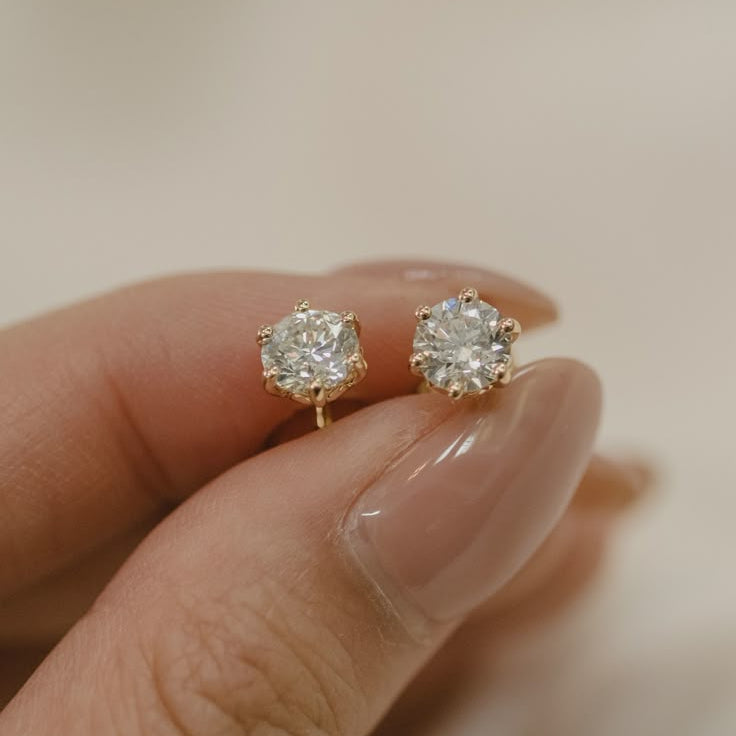 A pair of gold stud earrings, each featuring a round brilliant-cut diamond solitaire secured in a detailed six-prong setting.