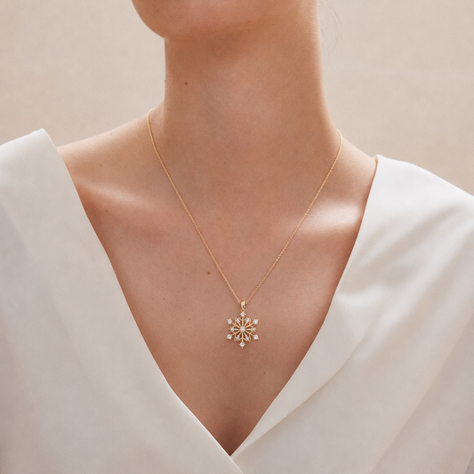 A yellow gold snowflake charm pendant featuring a central round diamond and smaller diamonds prong-set at the end of each branch against a white background.