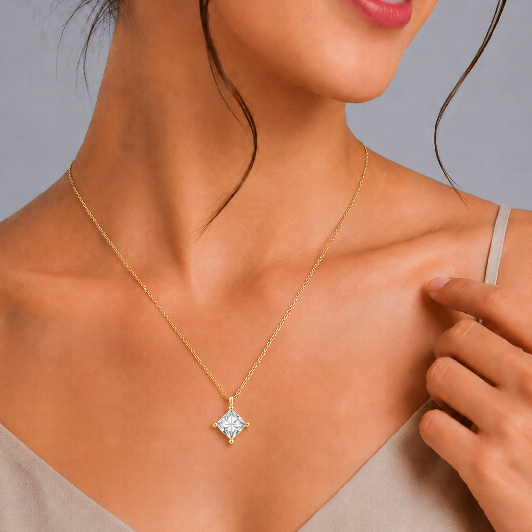 A yellow gold chain necklace featuring a single large princess-cut diamond solitaire pendant oriented in a kite setting, secured at the corners by minimalist gold prongs 