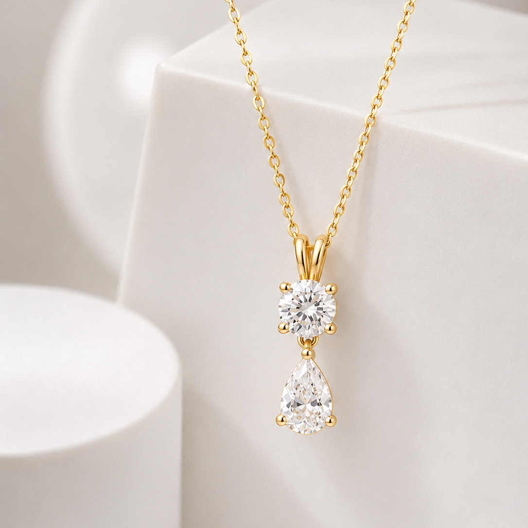 A yellow gold pendant necklace featuring two diamonds hanging vertically: a small round diamond at the top and a larger teardrop-shaped diamond below it.