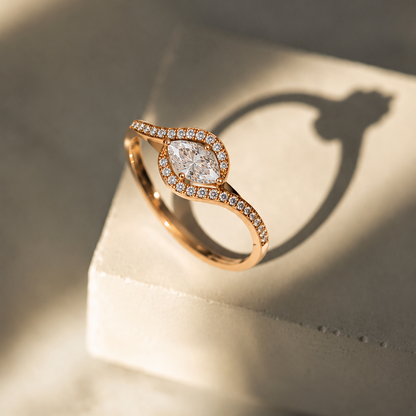 A rose gold ring featuring an eye-shaped marquise diamond center stone surrounded by a curved, diamond-lined twisting band.