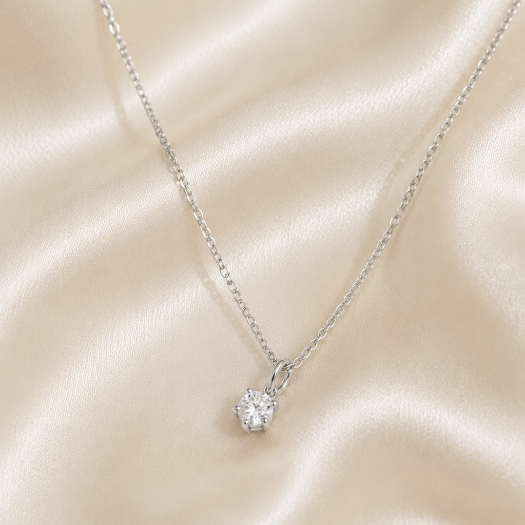 A silver necklace with a small, single round diamond pendant hanging in the center
