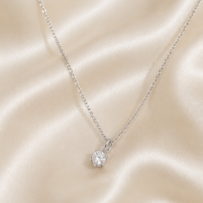 A silver necklace with a small, single round diamond pendant hanging in the center