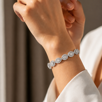 A silver link bracelet featuring alternating round and teardrop-shaped frames filled with sparkling baguette and round diamonds, resting on white silk.