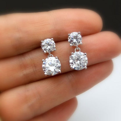 A pair of white gold or platinum drop earrings, each featuring two graduated round brilliant-cut diamonds stacked vertically in four-prong settings, connected by a small metal loop
